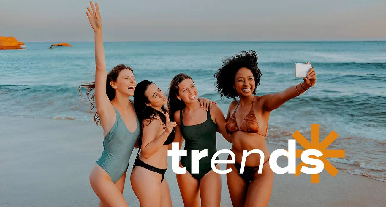 quatro mulheres com maiôs e biquínis tirando foto na praia, mostrando as tendências moda praia